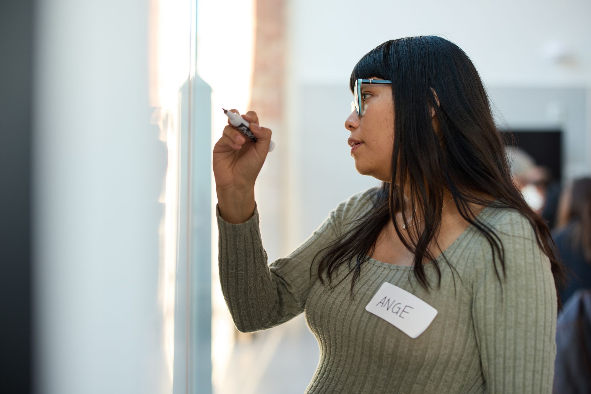 A close up of a participant in glasses writing on the whiteboard, backlit with an afternoon glow.